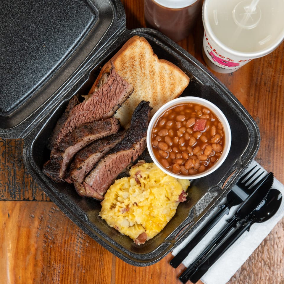 Blake's Barbecue brisket plate with baked beans, mashed potatoes, and Texas toast in a to-go container.