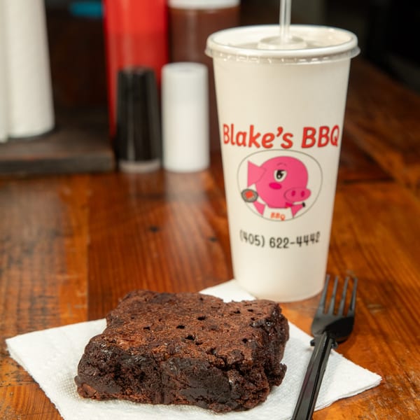 A Blake's BBQ branded drink cup and a chocolate brownie on a napkin with a fork.