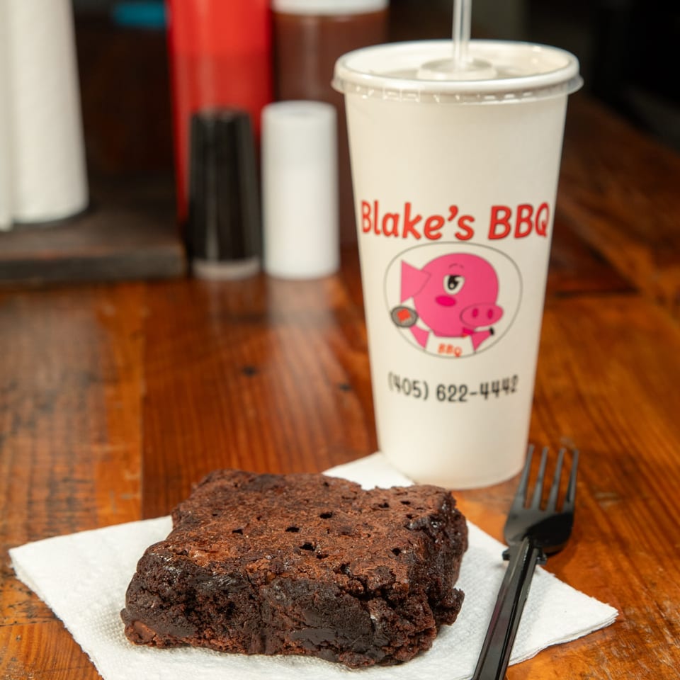 A Blake's BBQ branded drink cup and a chocolate brownie on a napkin with a fork.