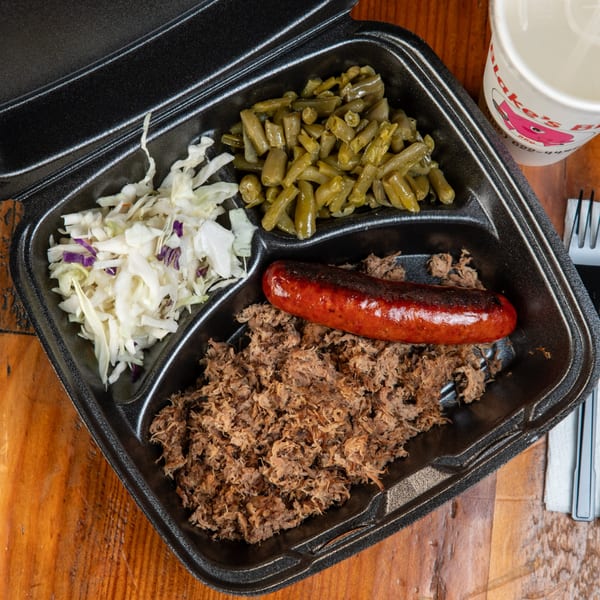 Blake's Barbecue takeout container with pulled pork, sausage, green beans, and coleslaw on a wooden table.