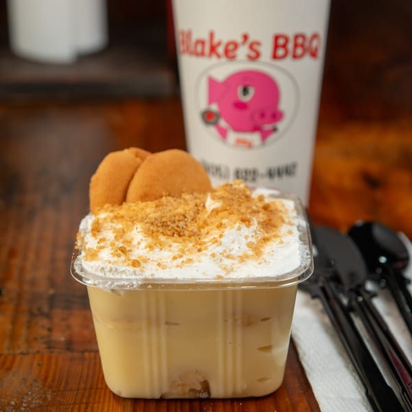 Banana pudding with whipped cream, cookie crumbles, and vanilla wafers, next to a Blake's BBQ cup.
