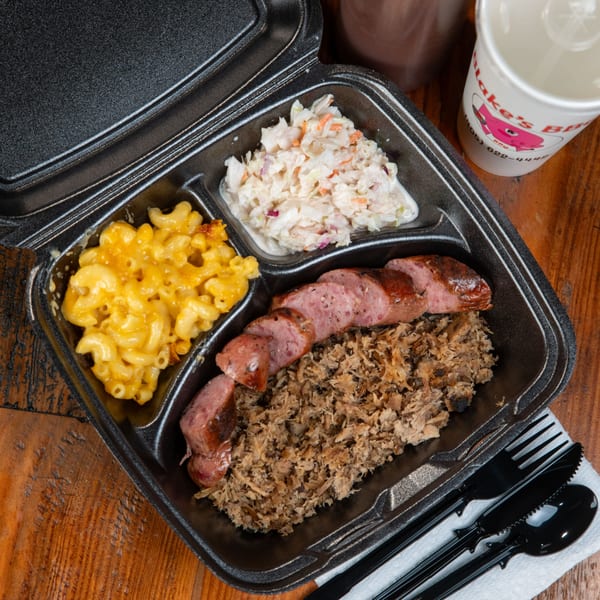 Blake's Barbecue takeout container with sliced sausage, pulled pork, mac and cheese, and coleslaw.