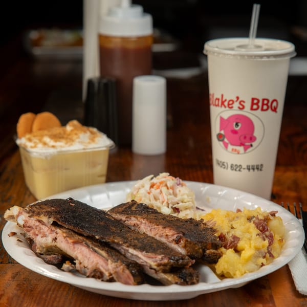 Blake's Barbecue ribs, coleslaw, and potato salad on a plate with a drink and banana pudding.